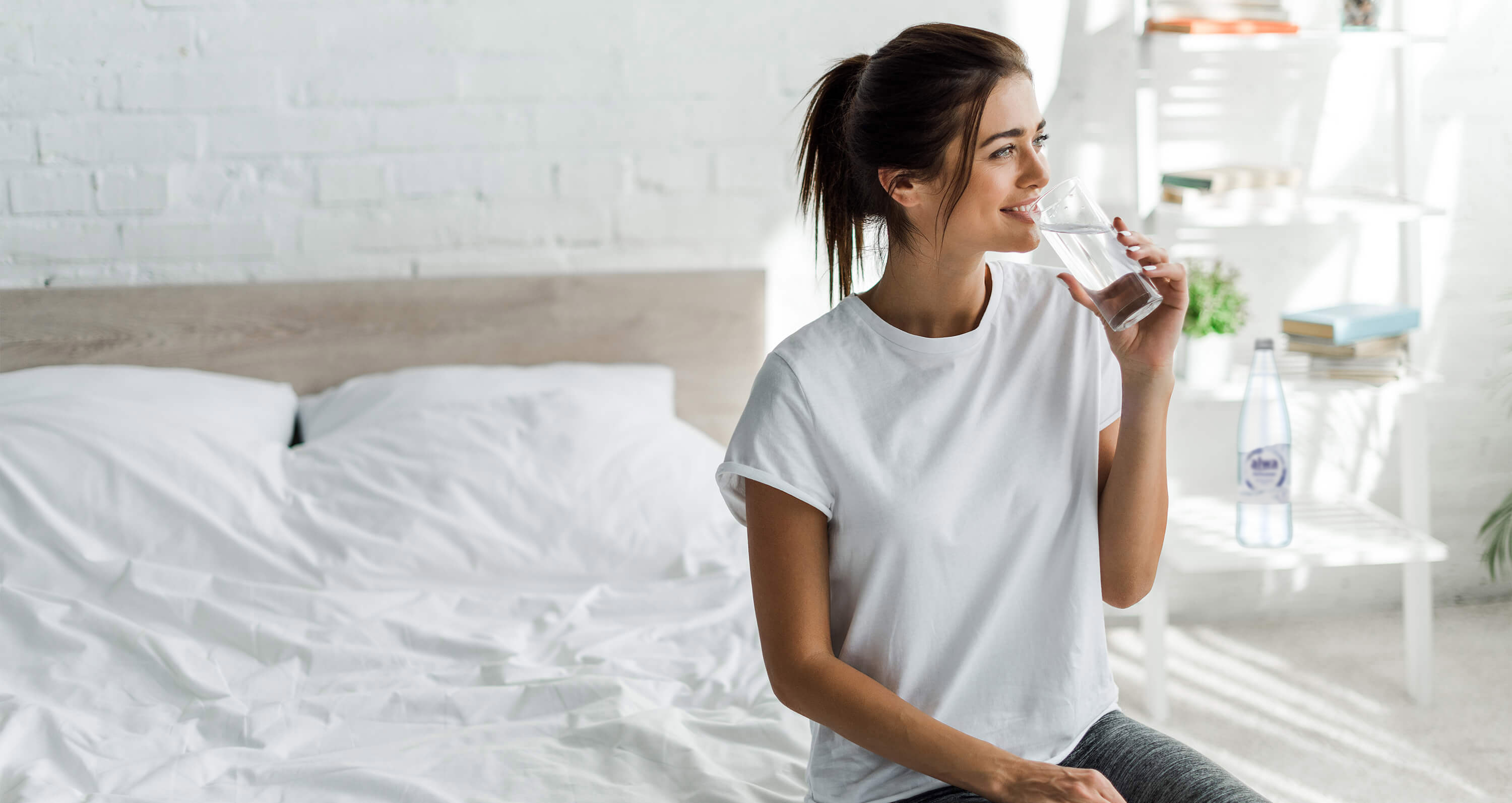 Frau sitzt auf Bett mit Glas Heilwasser in der Hand