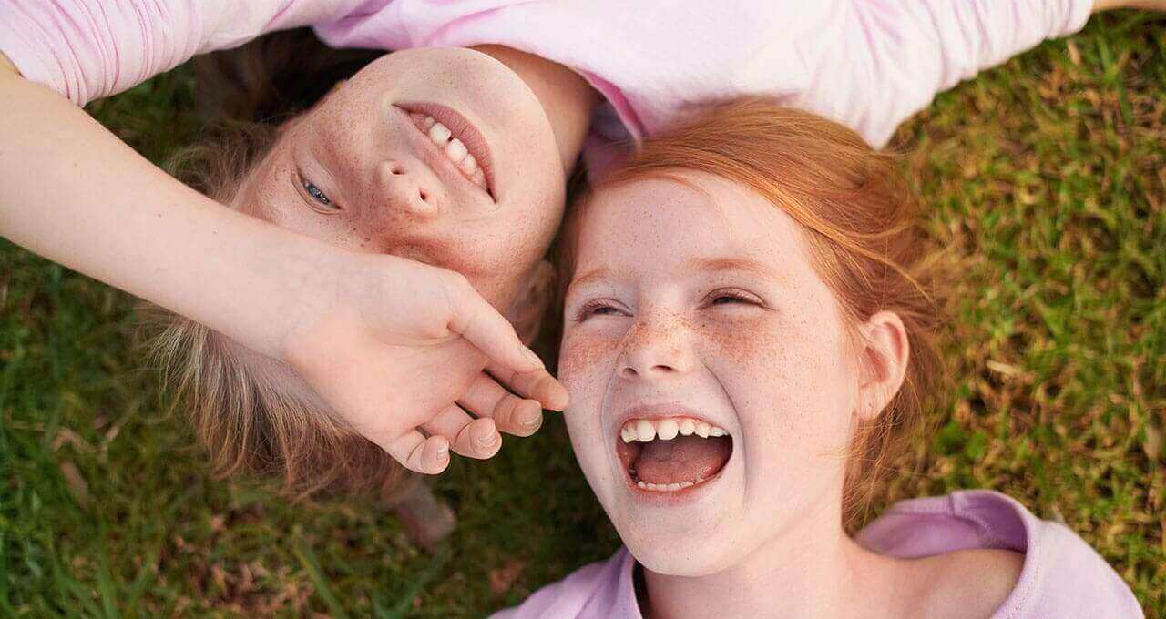 Zwei Mädels liegen lachend auf einer Wiese