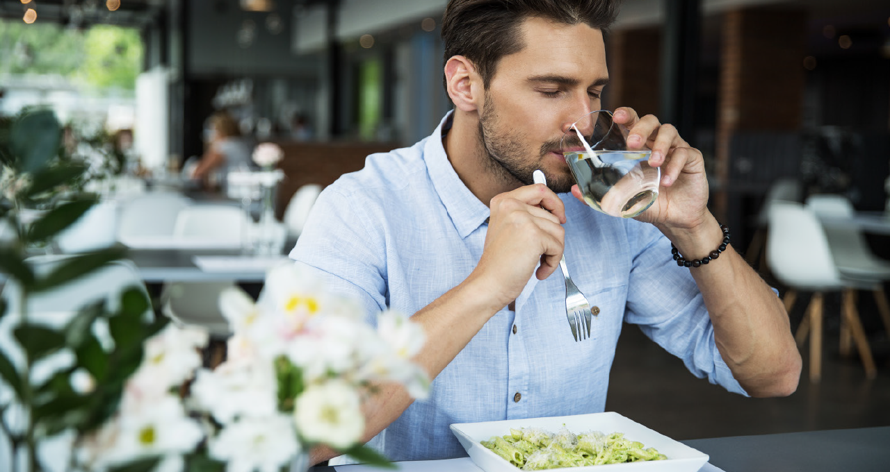 Mann trinkt aus Mineralwasserglas und isst Salat