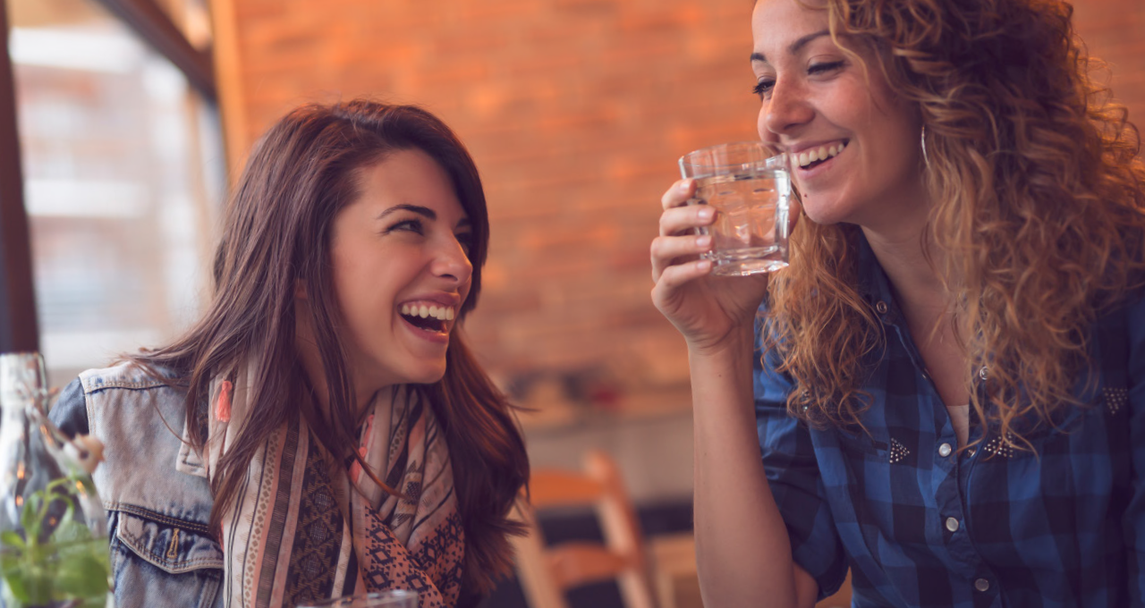 Lachende Frauen, eine mit Mineralwasserglas in der Hand