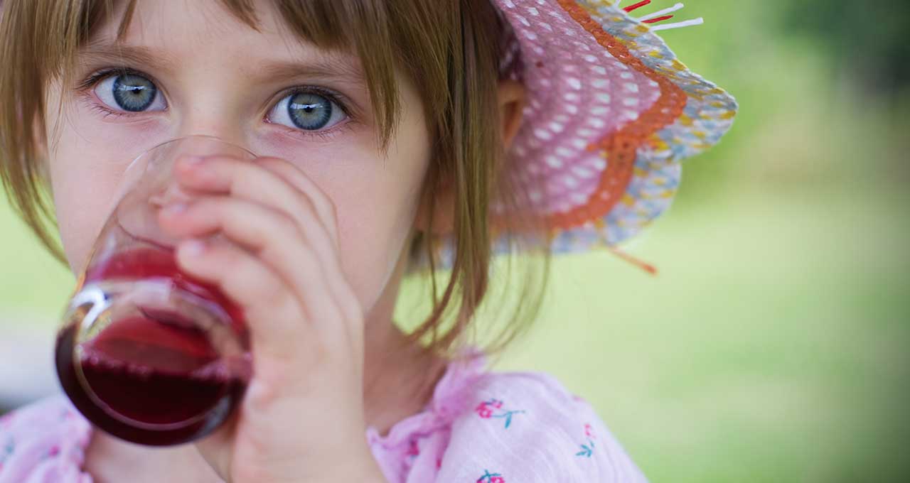 Mädchen mit Hut trinkt Johannisbeerschorle aus einem Glas