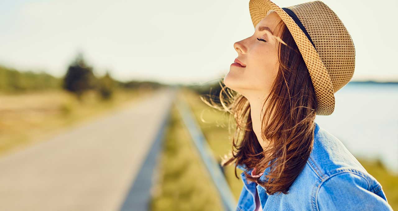 Frau mit Hut und geschlossenen Augen genießt die Sonne
