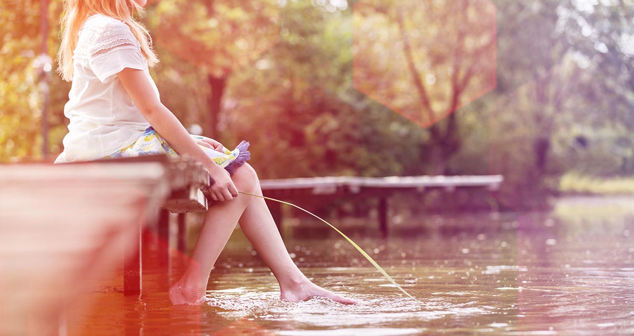 Mädchen sitzt auf Steg mit den Füßen im Wasser