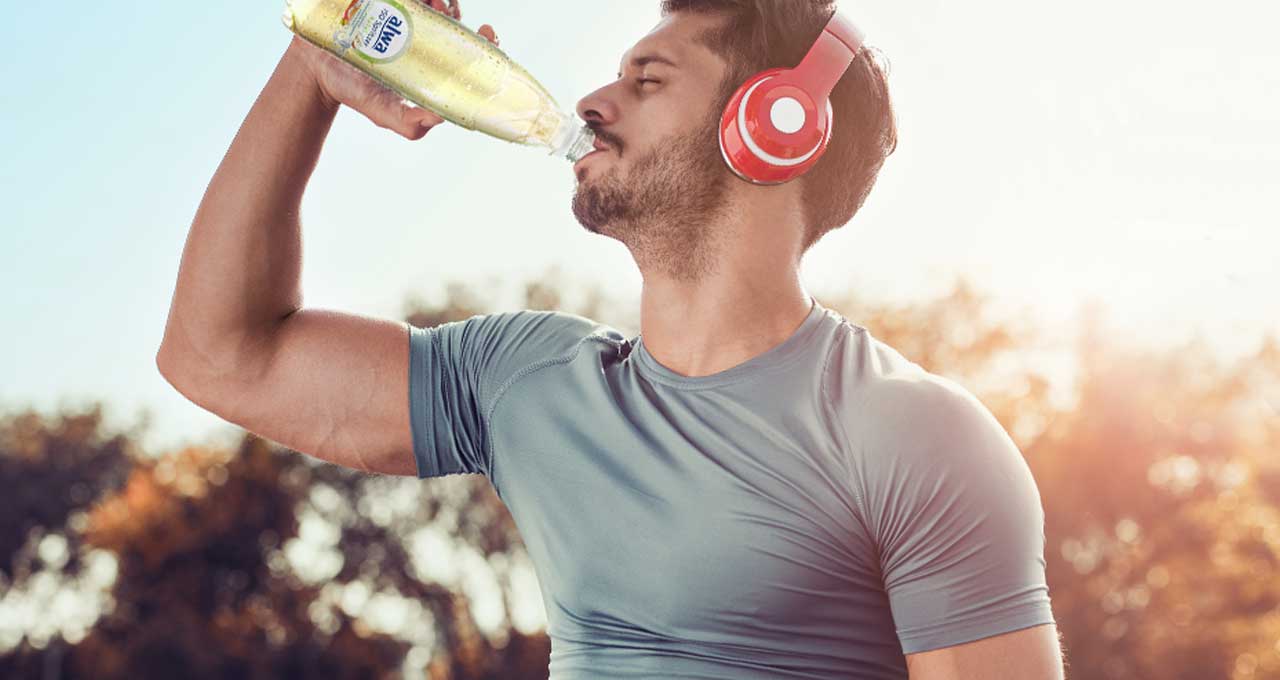 Mann mit Kopfhörern trinkt das Sportgetränk Apfel aus der Flasche