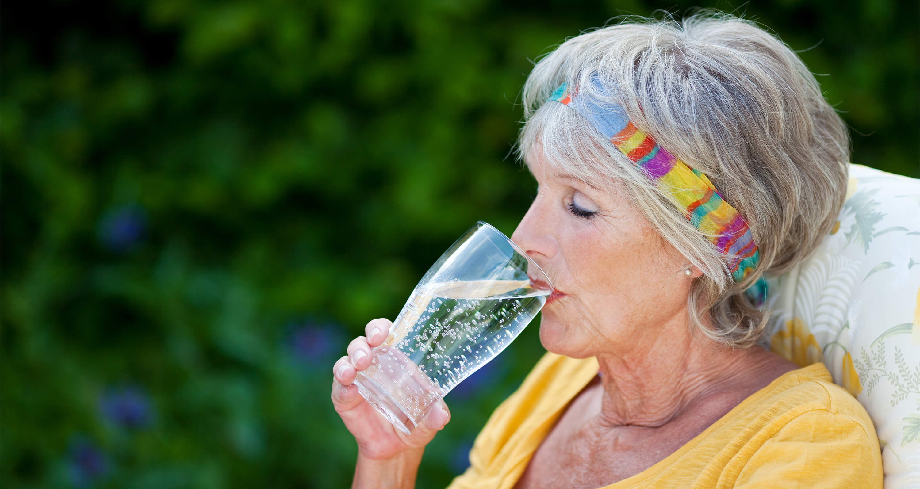 Frau mit buntem Stirnband trinkt aus Mineralwasserglas