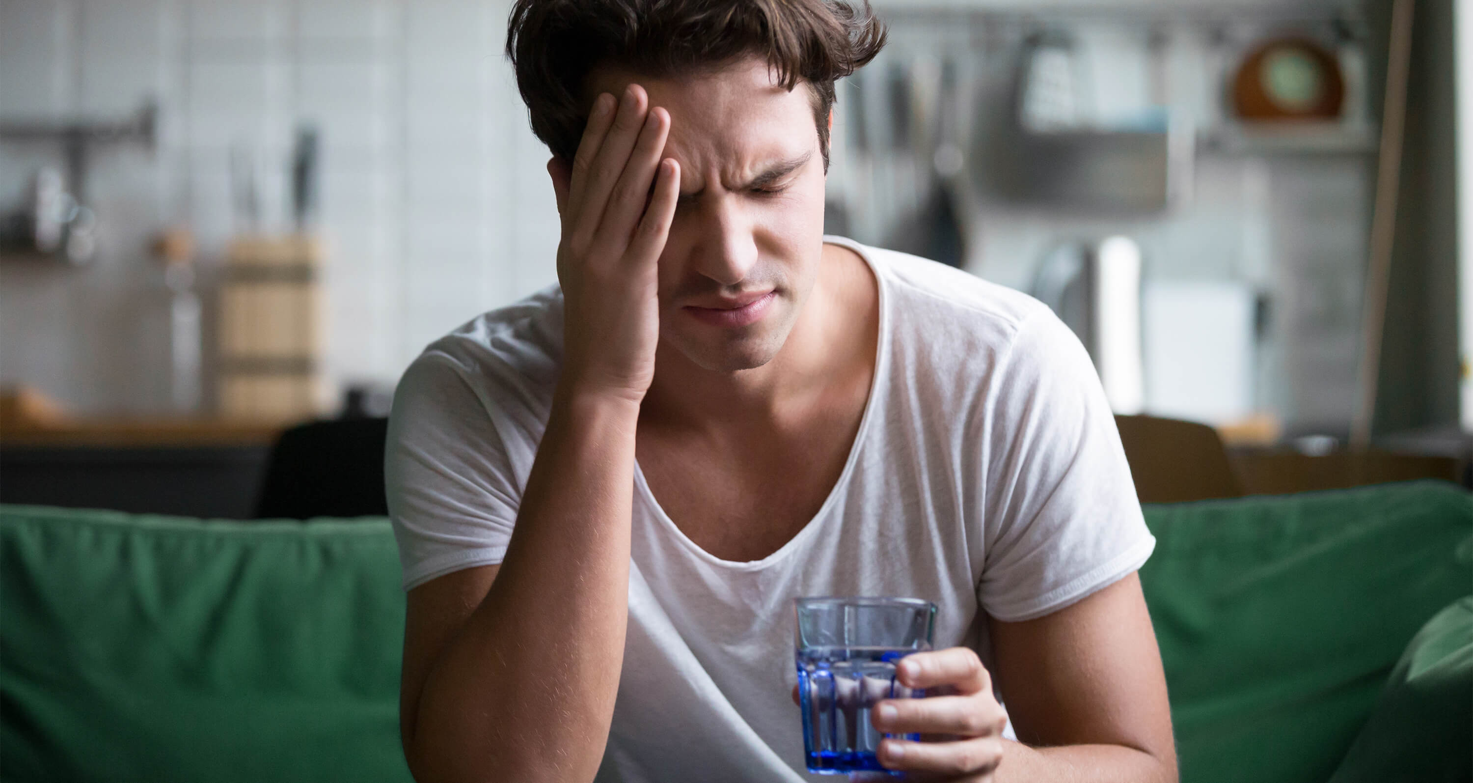 Mann mit Kopfschmerzen und Mineralwasserglas